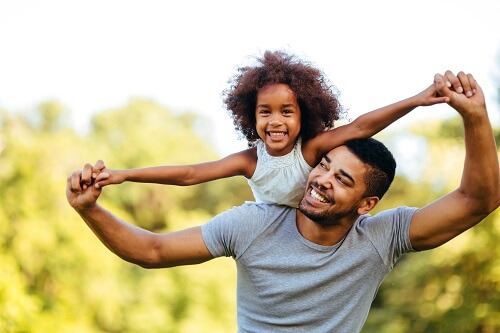 Father at a park with his daughter on his back.